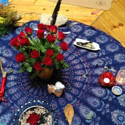 Red roses on a circular blue mandala altar cloth, a goddess fihuringe, some candles and other ritual objects