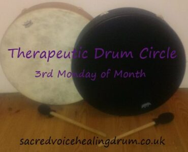 A black and a white drum intersected on a wooden floor with the words Therapeutic Drum Circle 3rd Monday of Month sacredvoicehealingdrum.co.uk